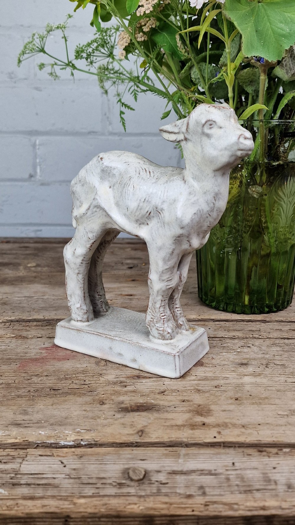 A cream glazed terracotta figurine depicting a standing kid goat mounted on a low rectangular base. View V