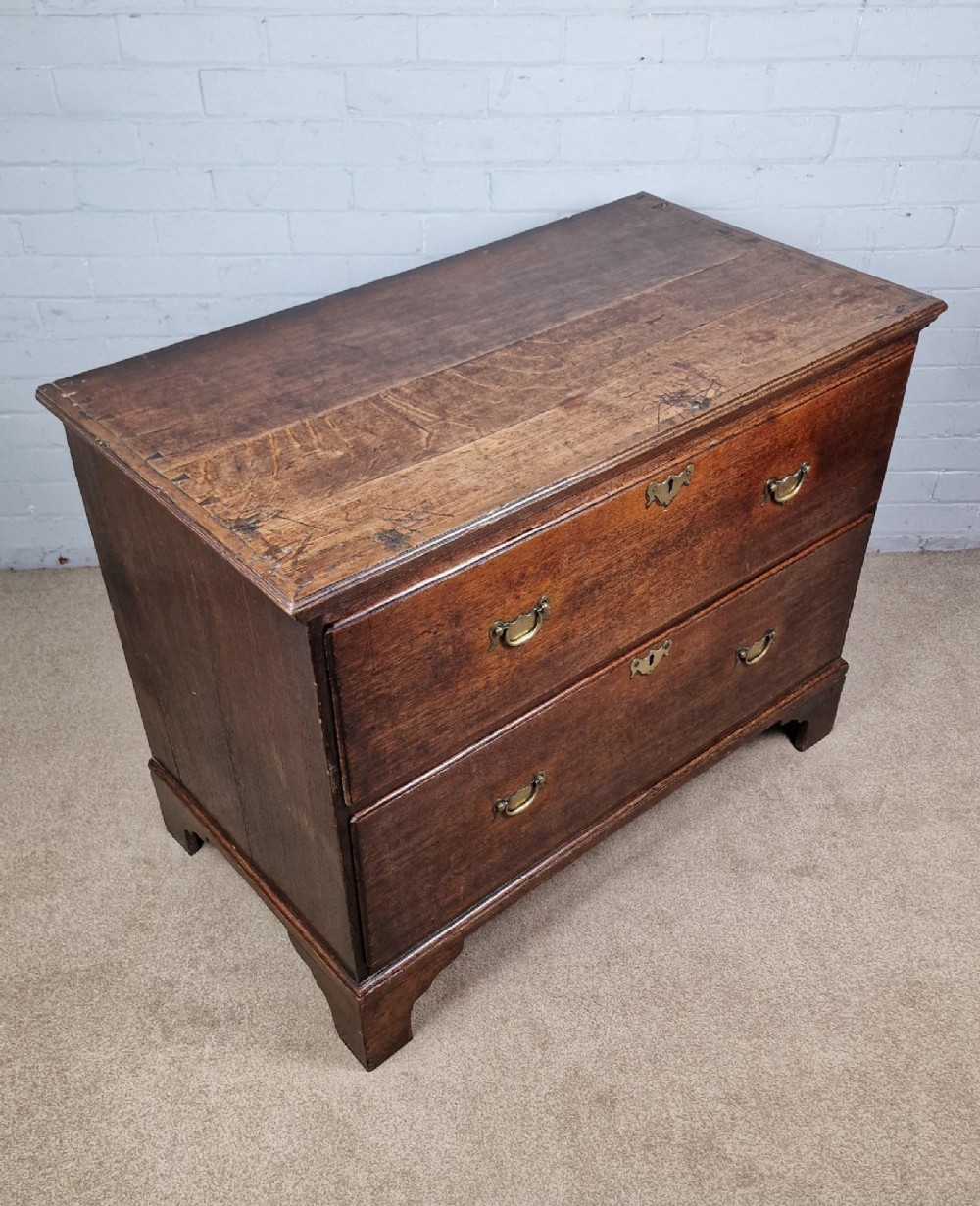 An 18th-century dark oak chest of drawers featuring two wide drawers with brass handles, standing on shaped bracket feet. View III