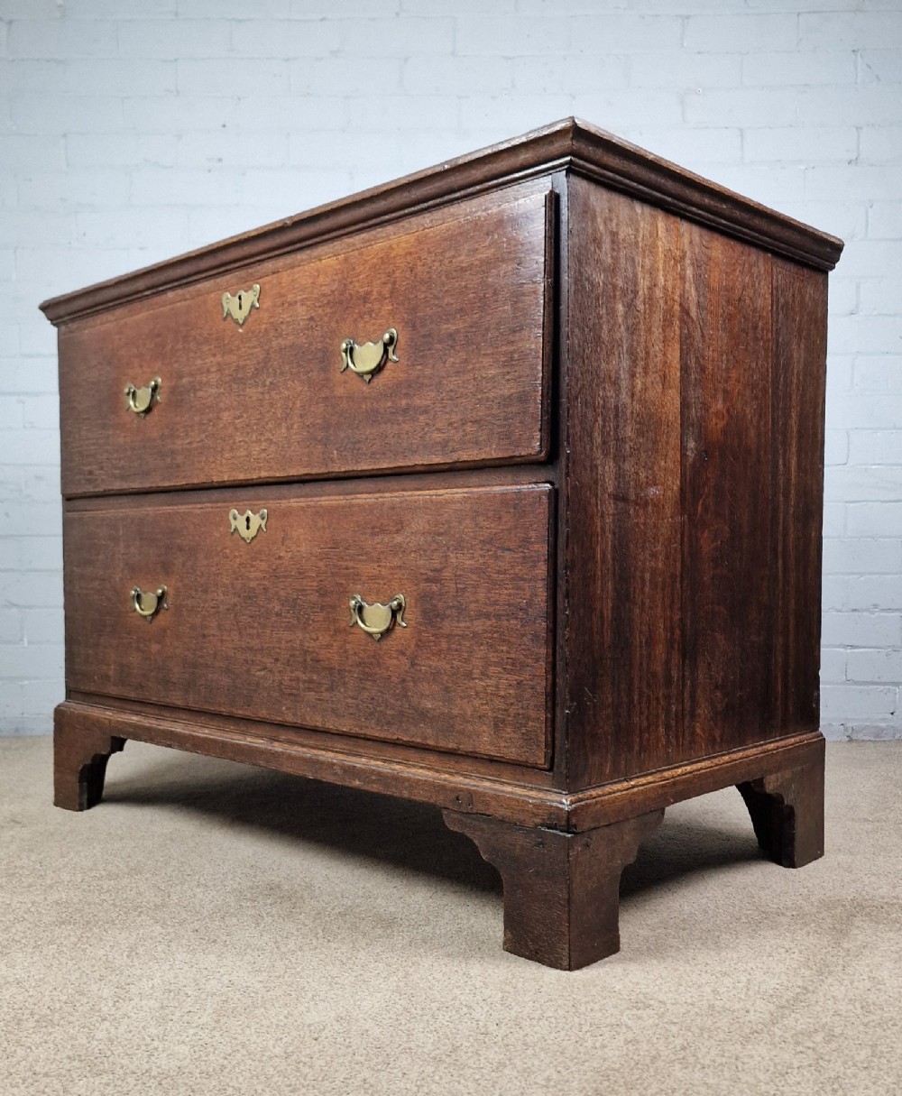 An 18th-century dark oak chest of drawers featuring two wide drawers with brass handles, standing on shaped bracket feet.