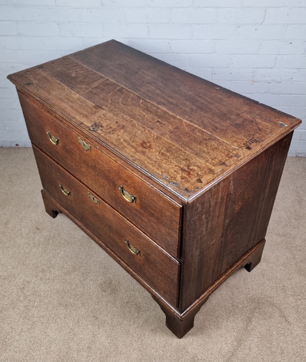 An 18th-century dark oak chest of drawers featuring two wide drawers with brass handles, standing on shaped bracket feet. View VI