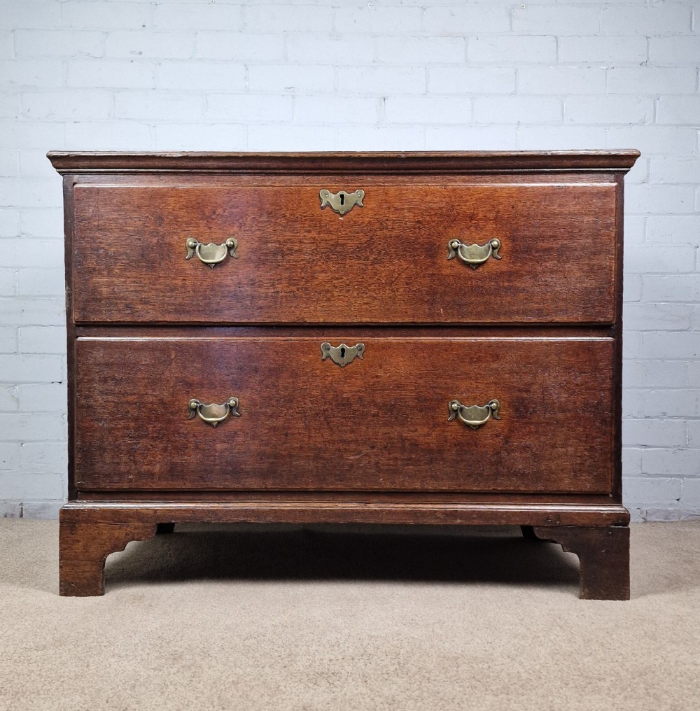 An 18th-century dark oak chest of drawers featuring two wide drawers with brass handles, standing on shaped bracket feet. View IX