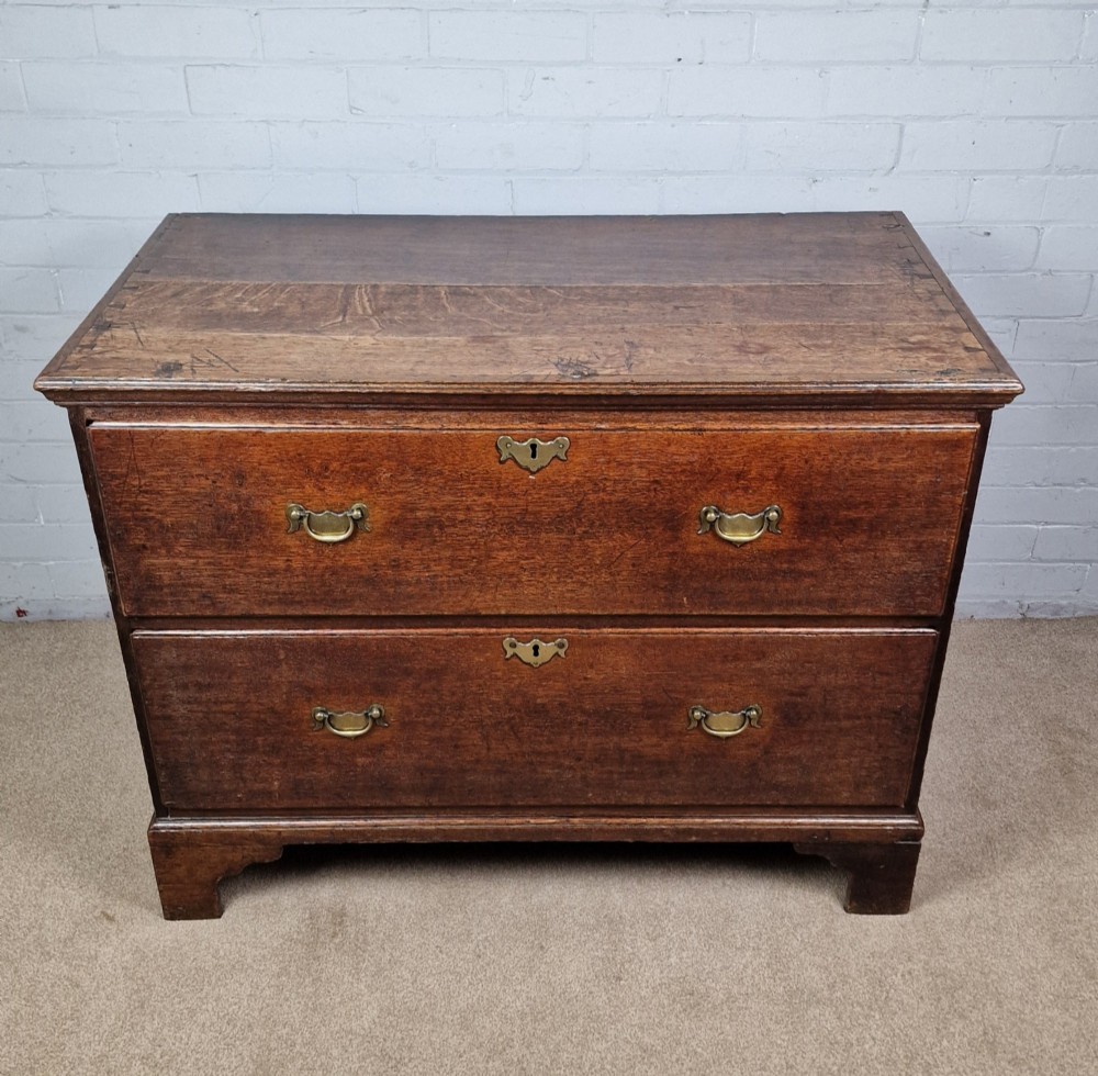 An 18th-century dark oak chest of drawers featuring two wide drawers with brass handles, standing on shaped bracket feet. View X