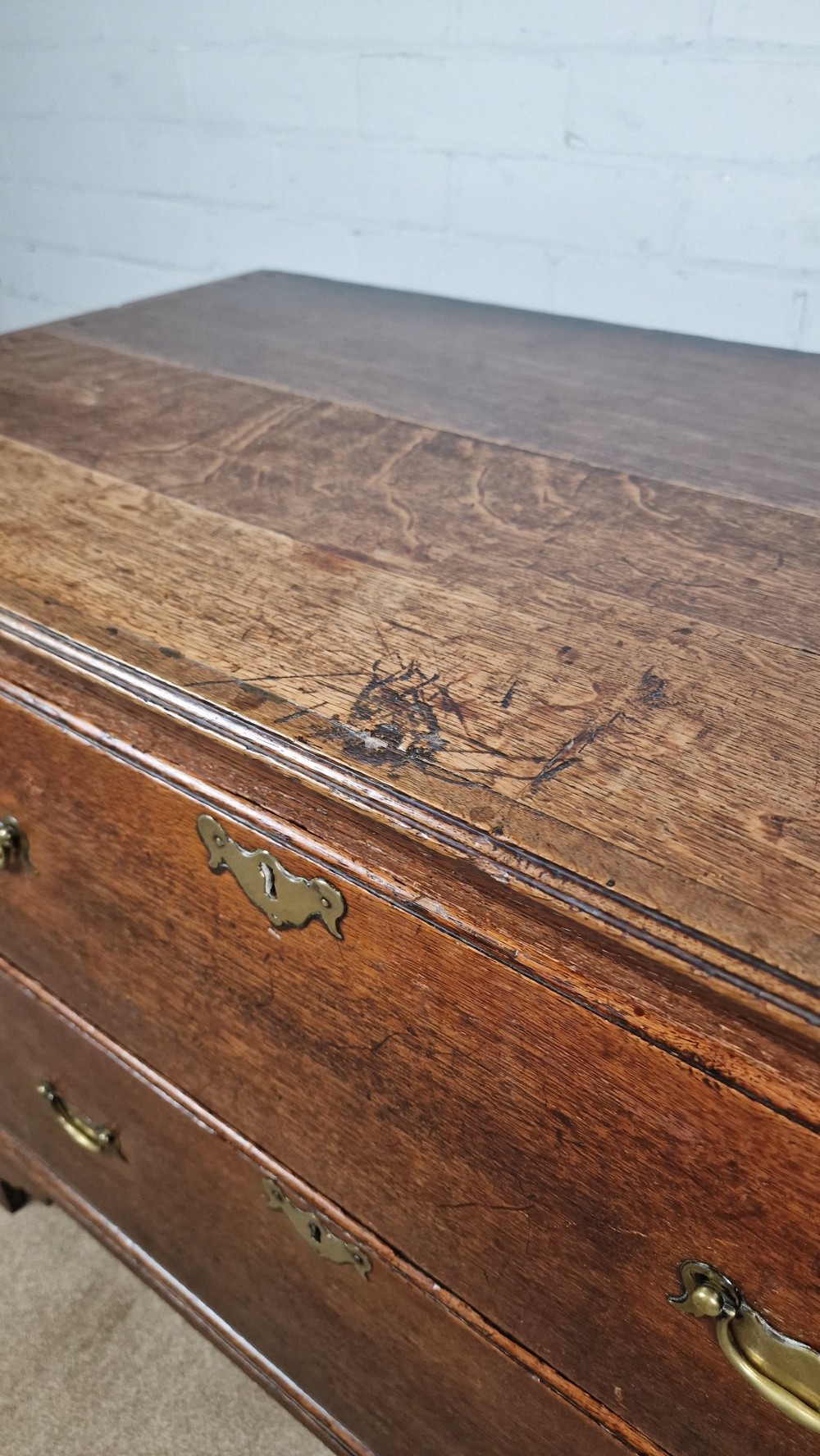 An 18th-century dark oak chest of drawers featuring two wide drawers with brass handles, standing on shaped bracket feet. View XI