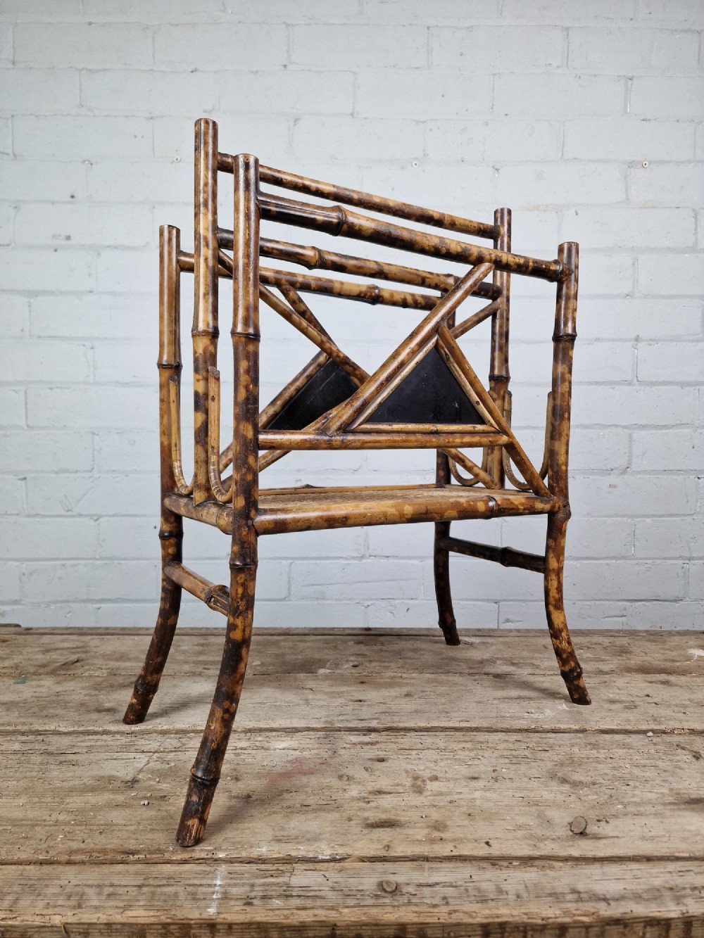 A late 19th-century Aesthetic Movement magazine rack crafted from scorched tortoiseshell bamboo with geometric triangular supports and black lacquered panels.
