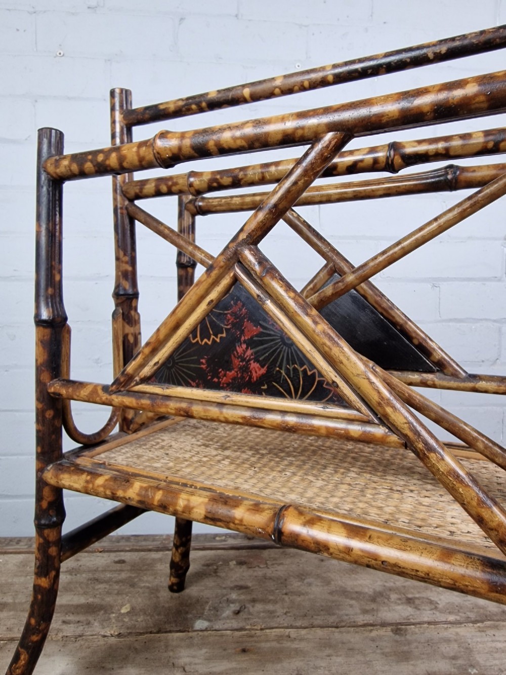 A late 19th-century Aesthetic Movement magazine rack crafted from scorched tortoiseshell bamboo with geometric triangular supports and black lacquered panels. View V