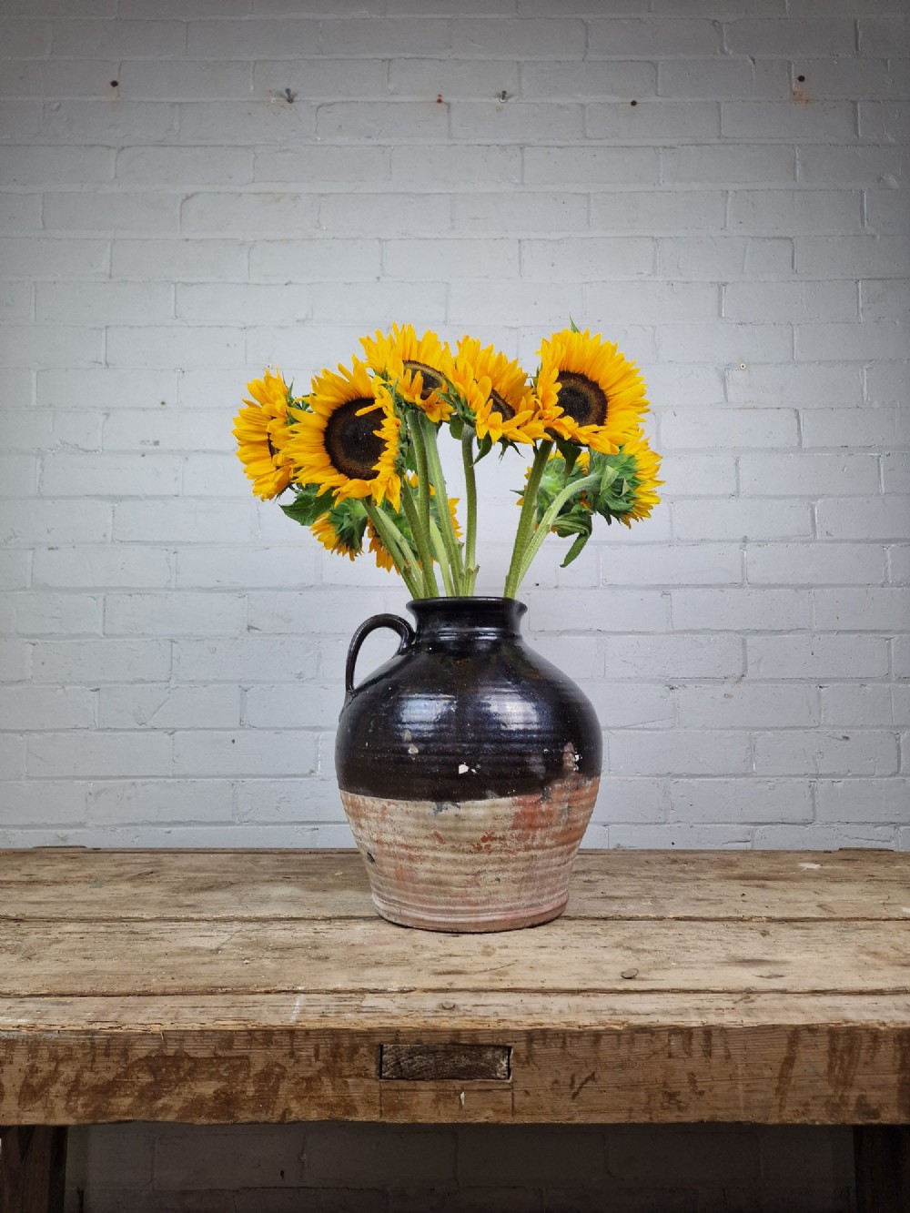 An antique late 18th or early 19th-century earthenware slipware jug featuring a dark brown glazed upper body and a textured terracotta lower base.