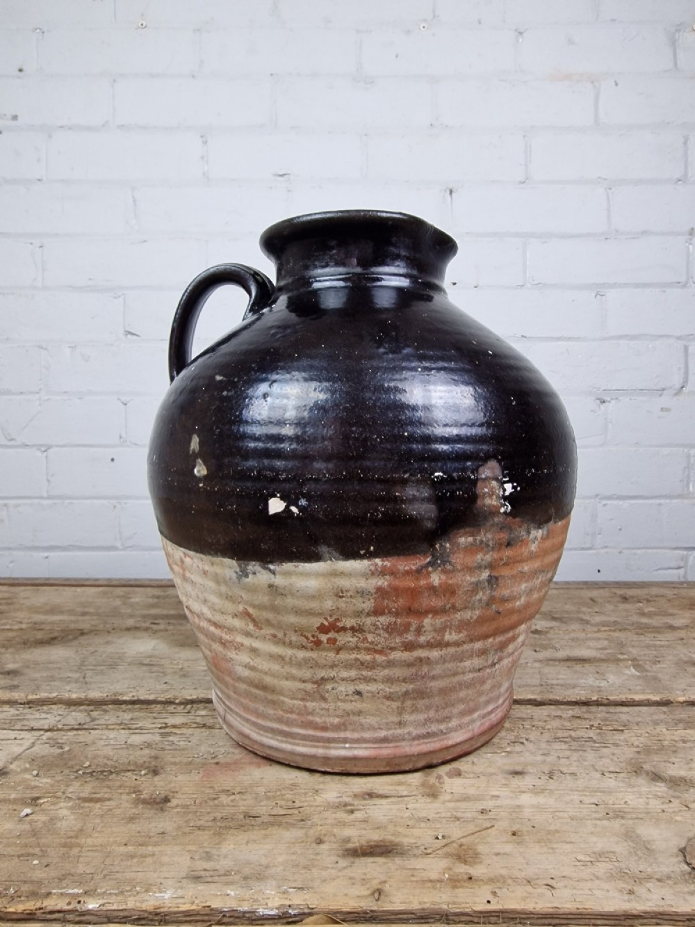 An antique late 18th or early 19th-century earthenware slipware jug featuring a dark brown glazed upper body and a textured terracotta lower base. View V