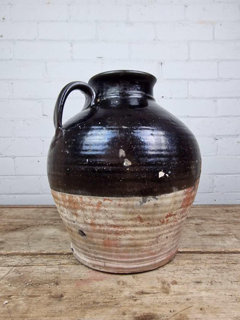 An antique late 18th or early 19th-century earthenware slipware jug featuring a dark brown glazed upper body and a textured terracotta lower base. View VI