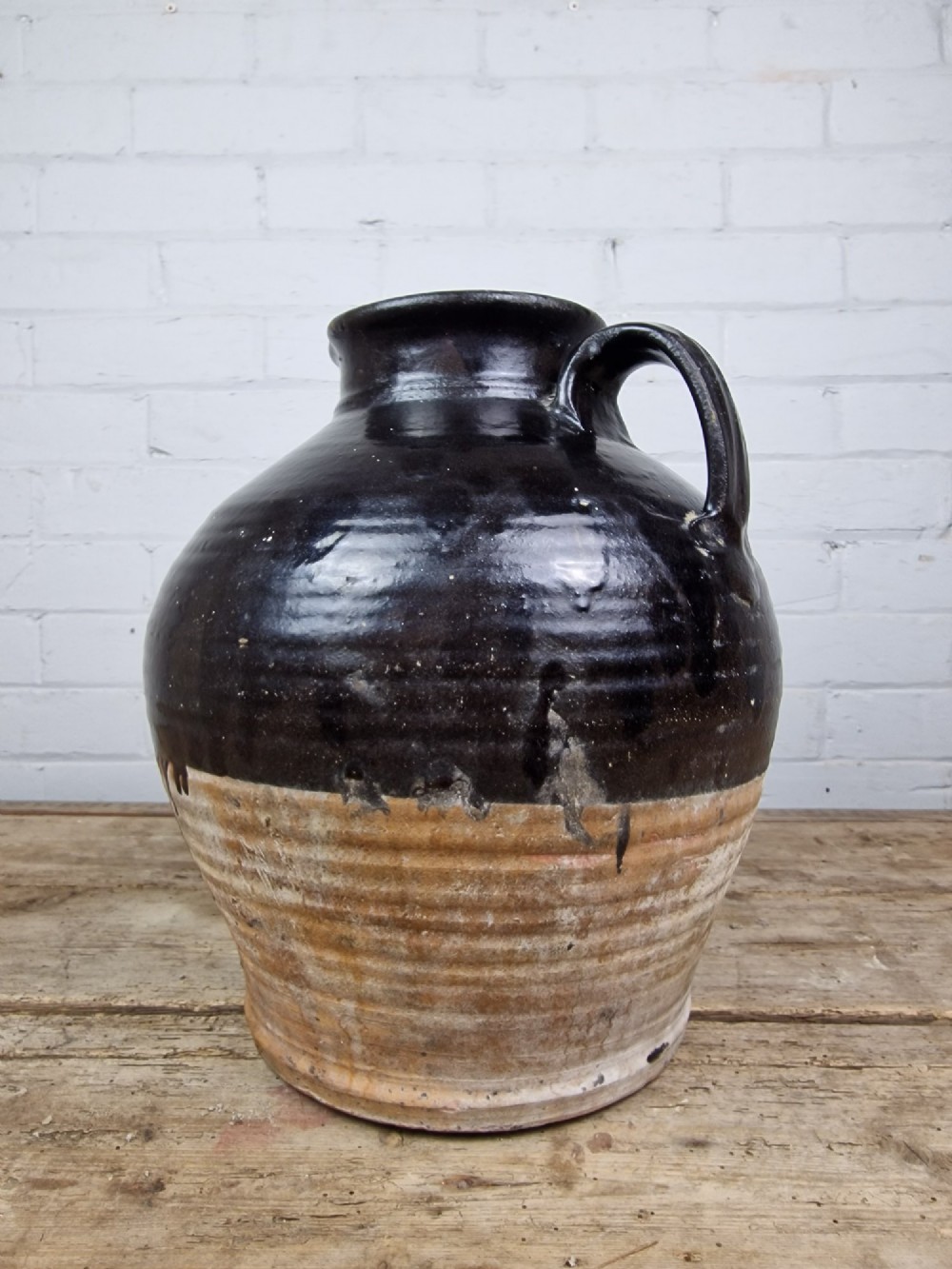 An antique late 18th or early 19th-century earthenware slipware jug featuring a dark brown glazed upper body and a textured terracotta lower base. View IX