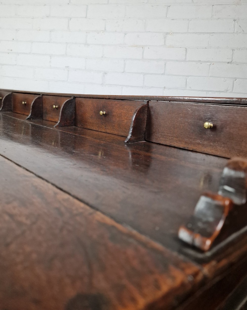 An antique dark oak dresser base featuring three upper drawers above two fielded panel cupboard doors with brass drop handles and a stepped upper gallery. View III
