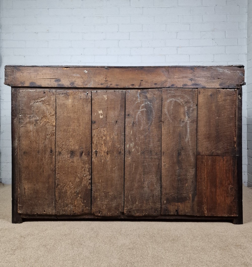 An antique dark oak dresser base featuring three upper drawers above two fielded panel cupboard doors with brass drop handles and a stepped upper gallery. View VI