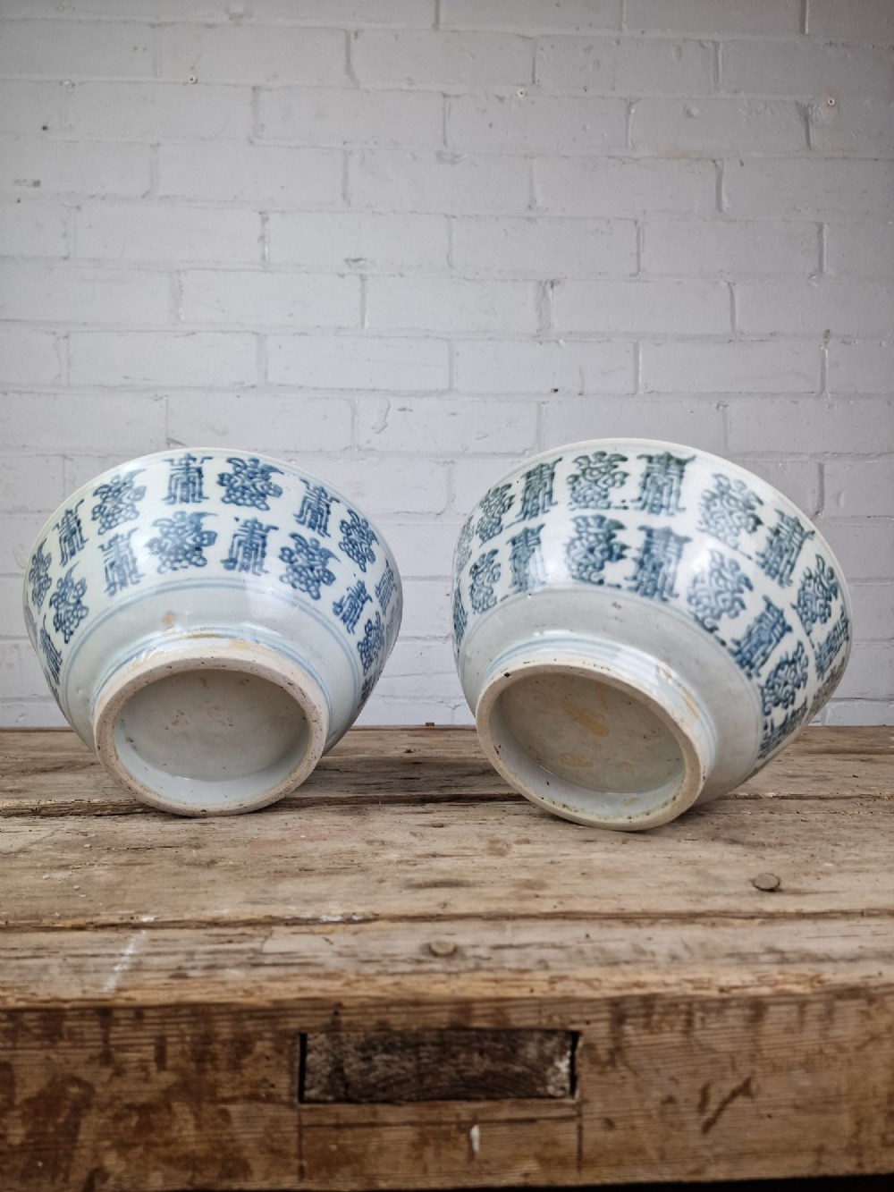 A pair of round Chinese provincial porcelain bowls featuring underglaze blue character motifs around the exterior on an off-white surface. View II