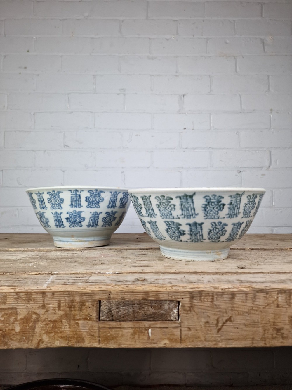 A pair of round Chinese provincial porcelain bowls featuring underglaze blue character motifs around the exterior on an off-white surface.