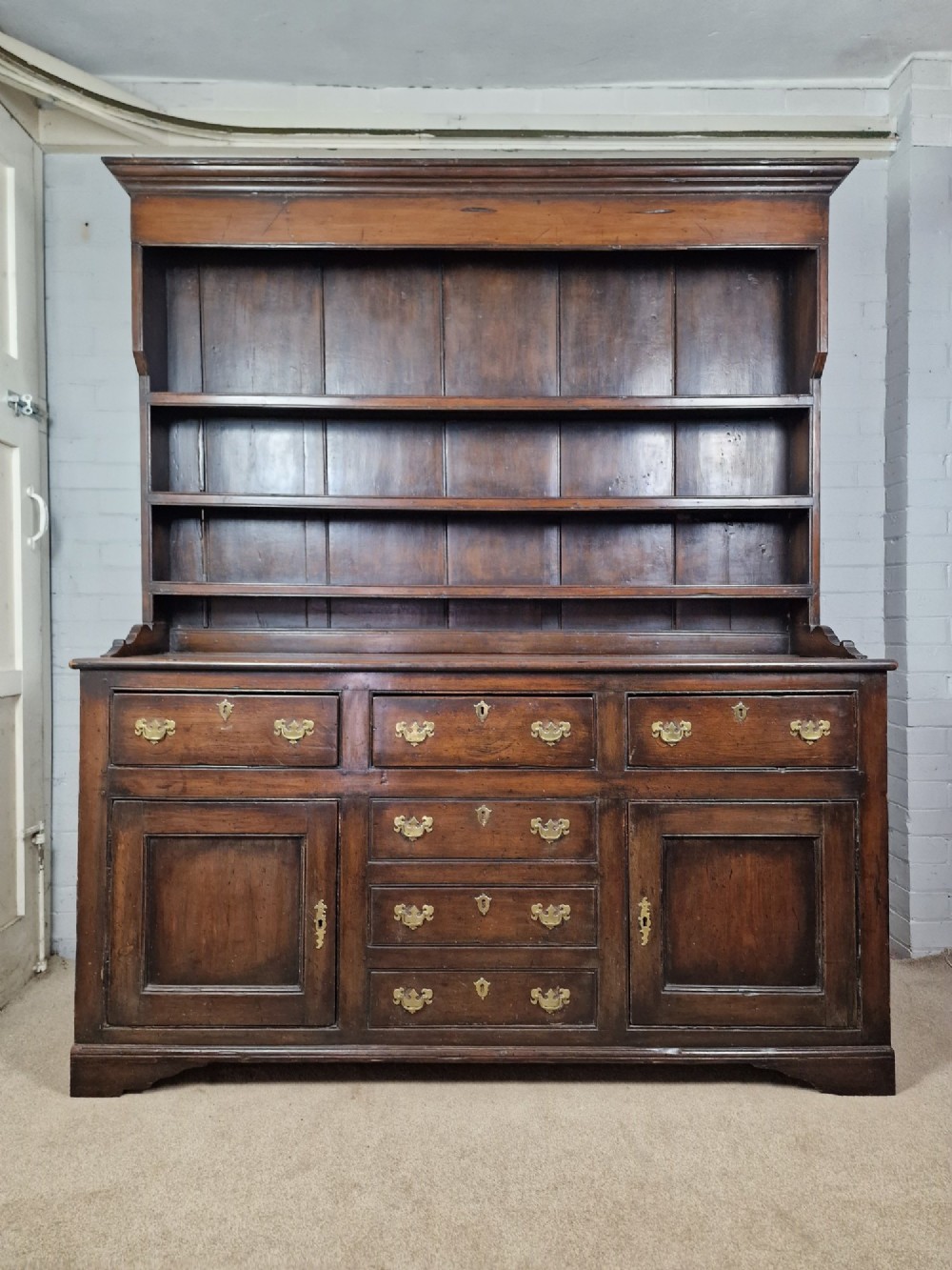 An antique dark oak dresser featuring a three-shelf open plate rack mounted above a base with multiple drawers and lower panelled cupboard doors. View II