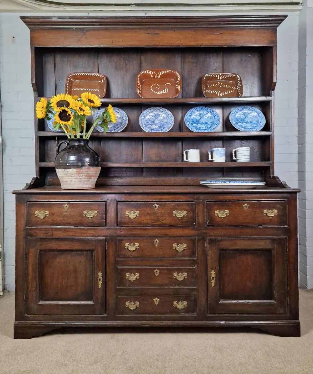 An antique dark oak dresser featuring a three-shelf open plate rack mounted above a base with multiple drawers and lower panelled cupboard doors.