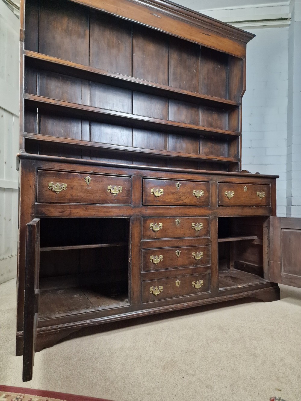 An antique dark oak dresser featuring a three-shelf open plate rack mounted above a base with multiple drawers and lower panelled cupboard doors. View V