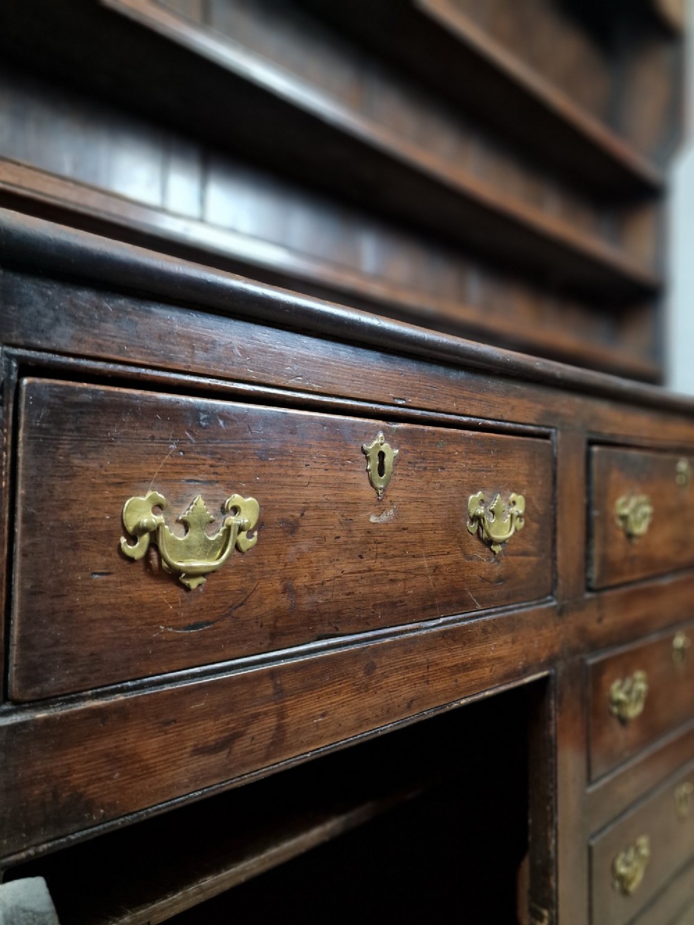 An antique dark oak dresser featuring a three-shelf open plate rack mounted above a base with multiple drawers and lower panelled cupboard doors. View VI