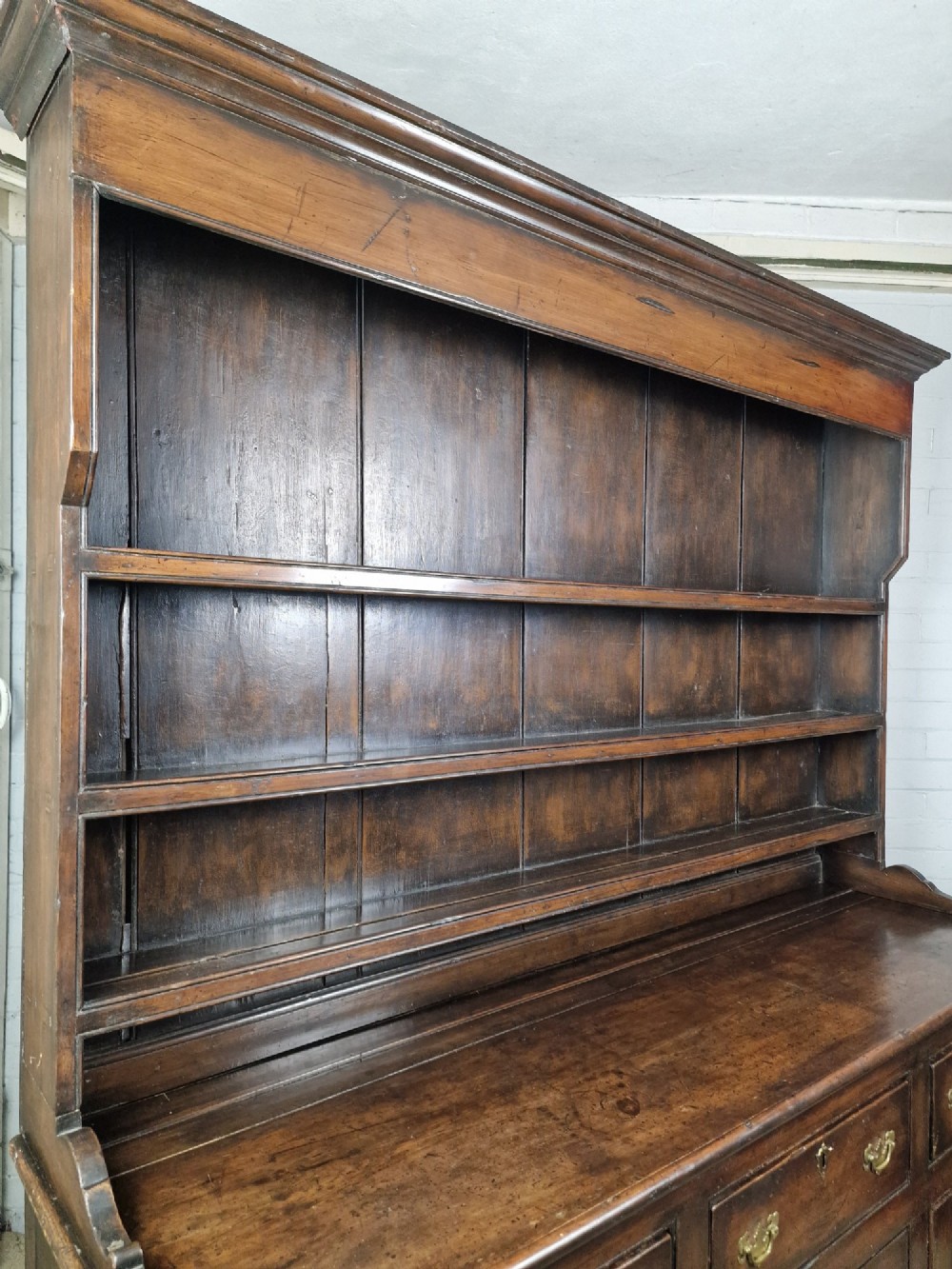 An antique dark oak dresser featuring a three-shelf open plate rack mounted above a base with multiple drawers and lower panelled cupboard doors. View VII
