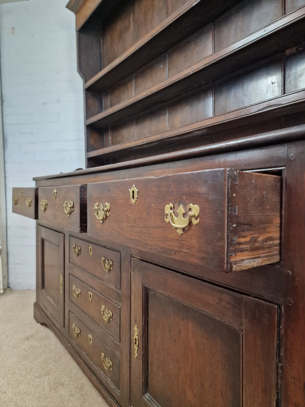 An antique dark oak dresser featuring a three-shelf open plate rack mounted above a base with multiple drawers and lower panelled cupboard doors. View VIII