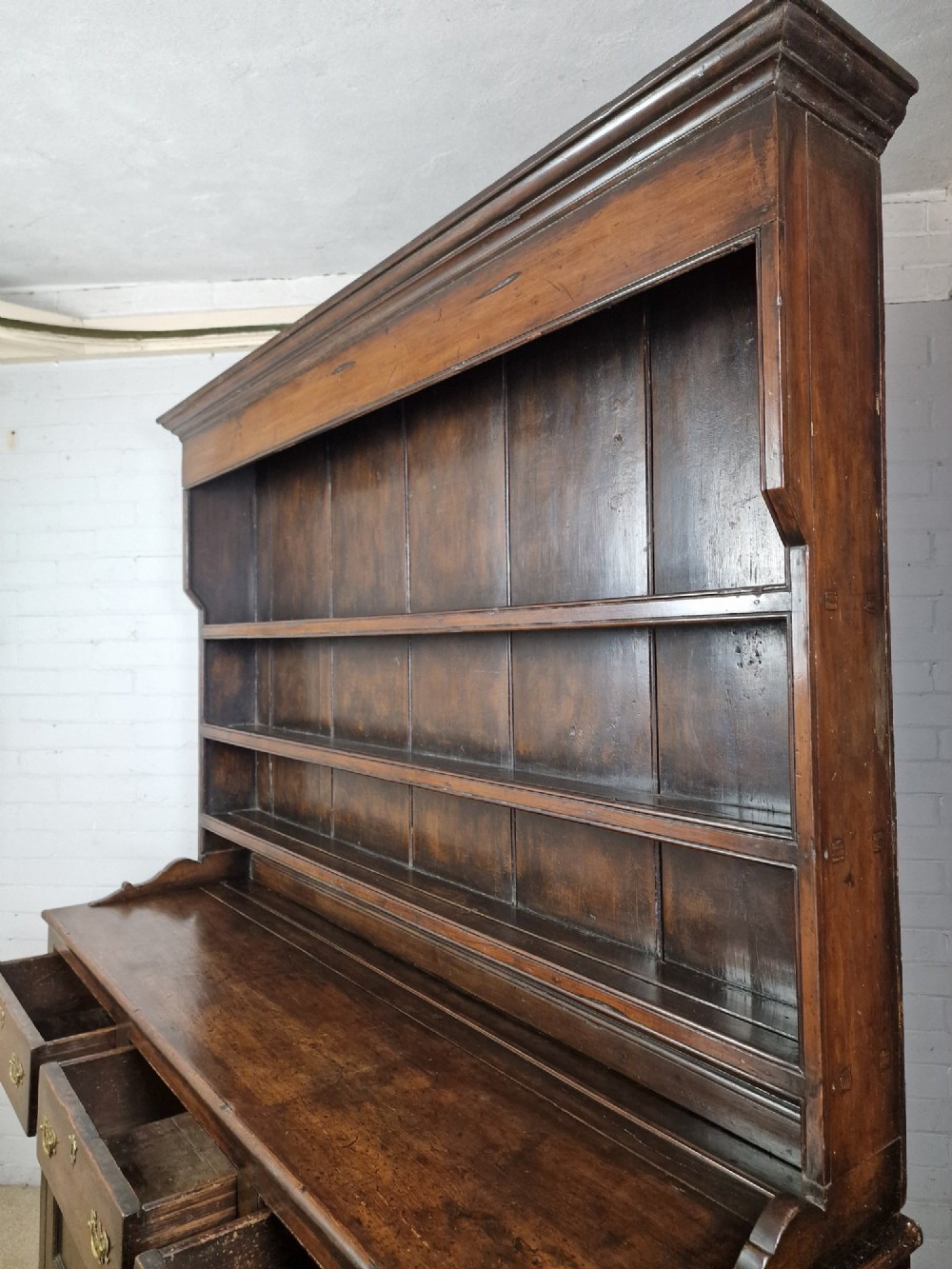 An antique dark oak dresser featuring a three-shelf open plate rack mounted above a base with multiple drawers and lower panelled cupboard doors. View IX