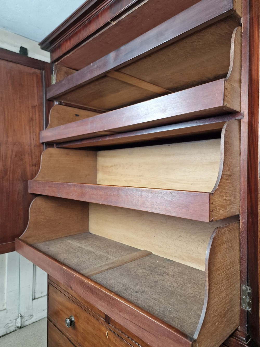 An early nineteenth-century George IV flame mahogany linen press featuring a double-door upper cupboard over a chest of drawers with bracket feet. View II