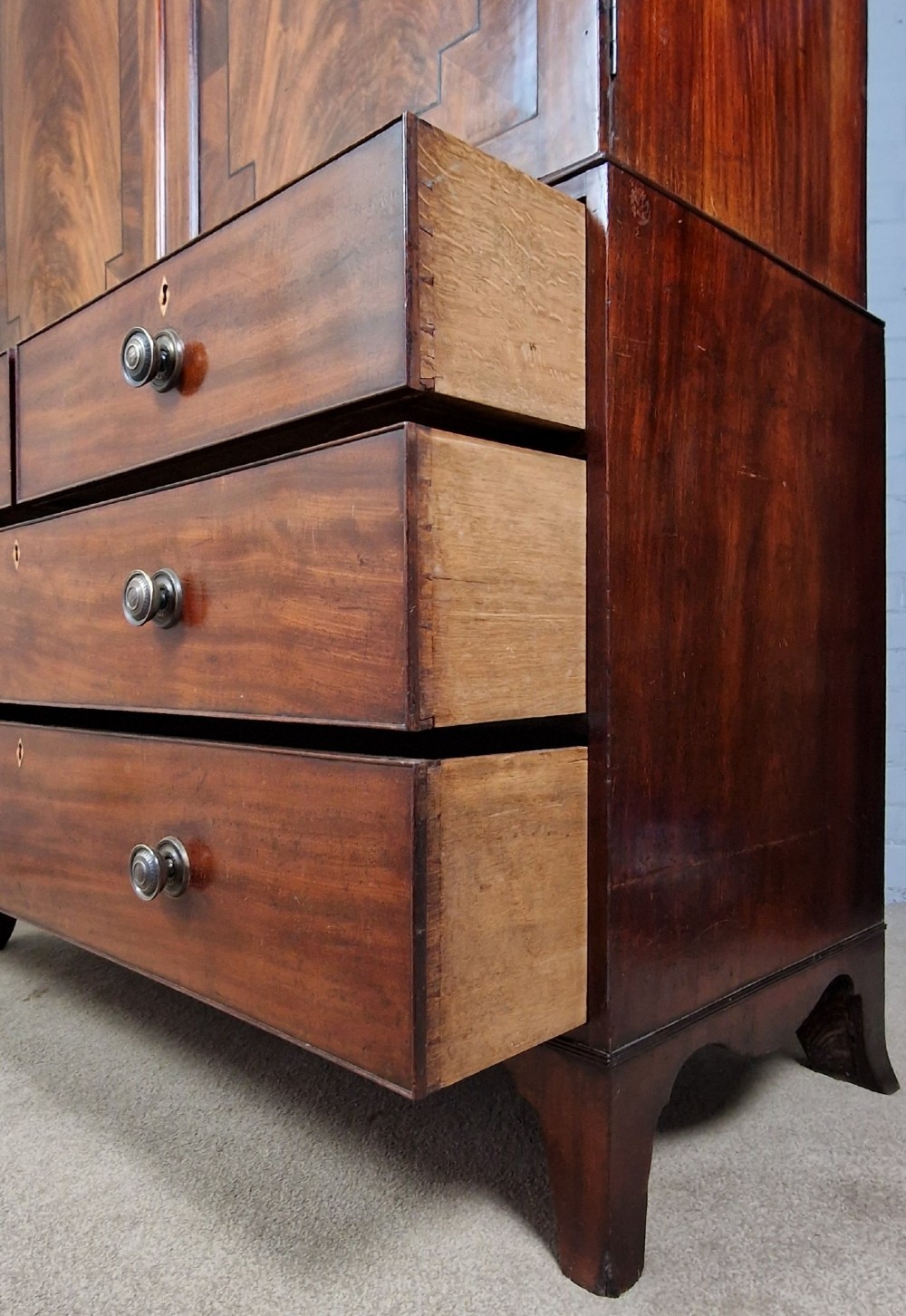 An early nineteenth-century George IV flame mahogany linen press featuring a double-door upper cupboard over a chest of drawers with bracket feet. View V