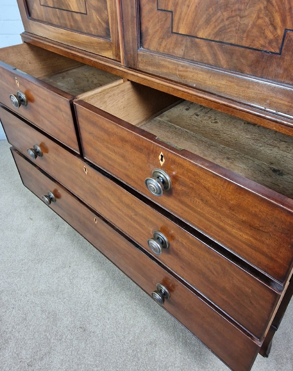 An early nineteenth-century George IV flame mahogany linen press featuring a double-door upper cupboard over a chest of drawers with bracket feet. View VI