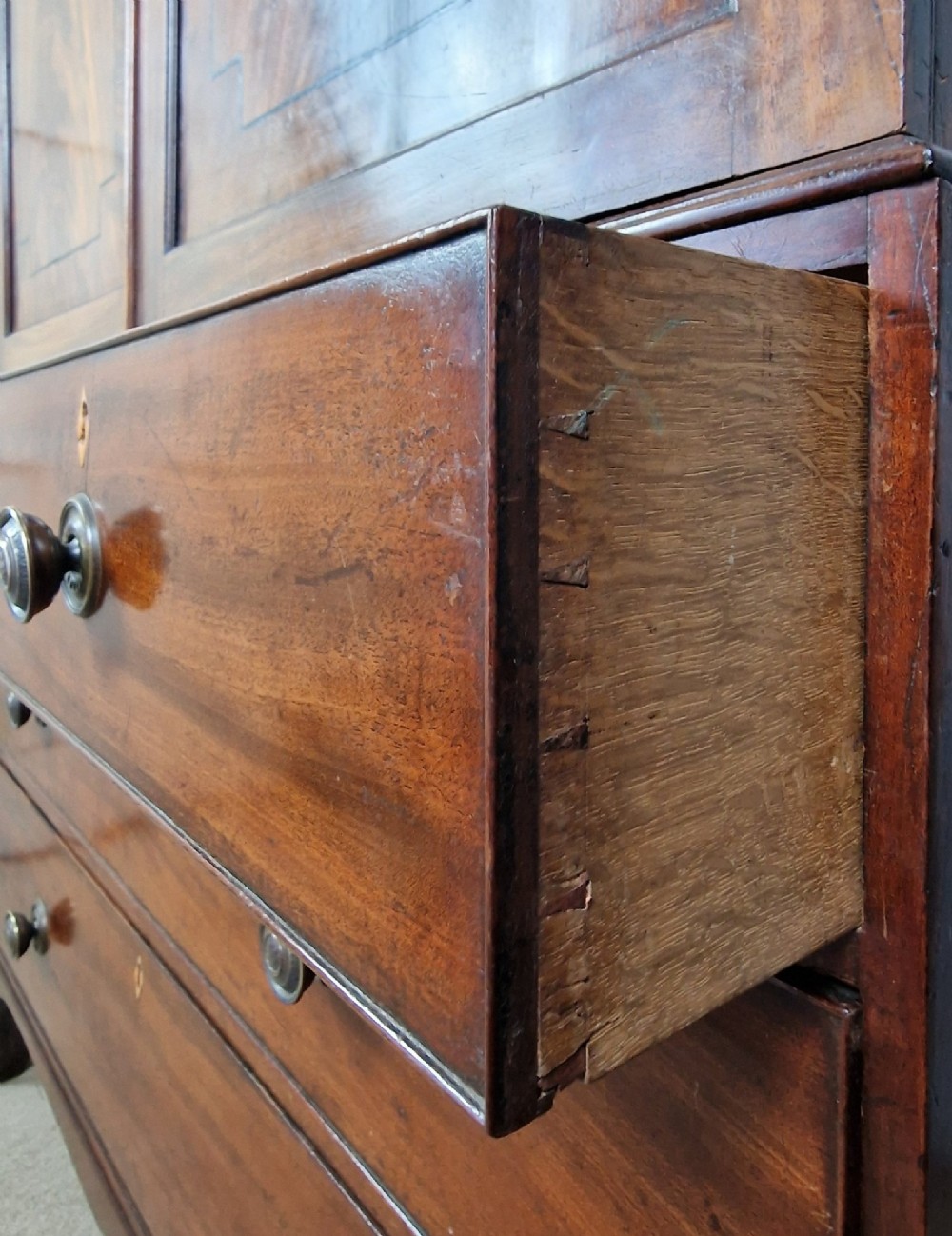 An early nineteenth-century George IV flame mahogany linen press featuring a double-door upper cupboard over a chest of drawers with bracket feet. View IX