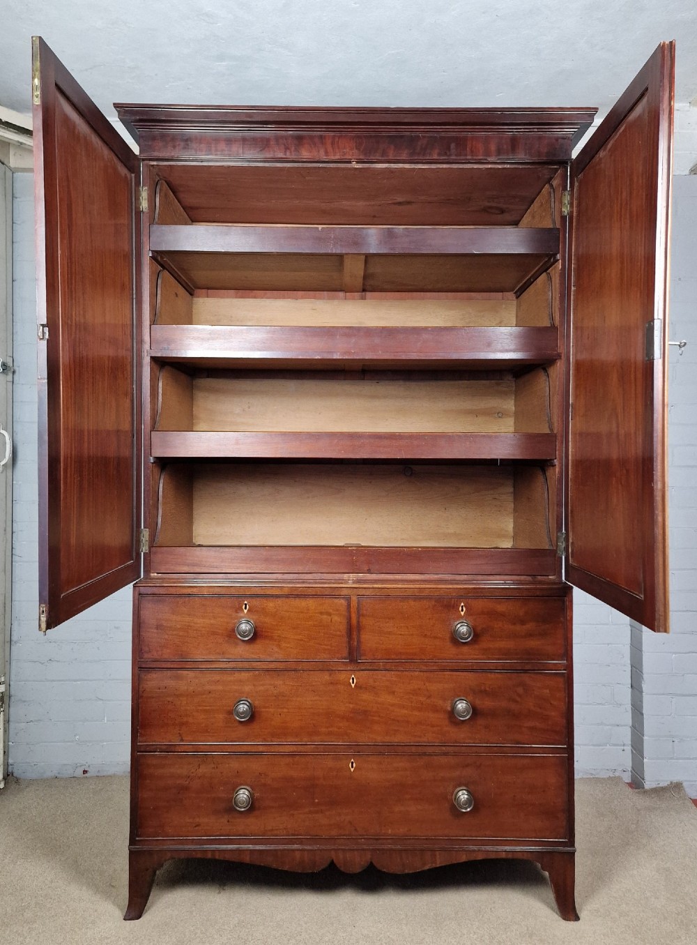 An early nineteenth-century George IV flame mahogany linen press featuring a double-door upper cupboard over a chest of drawers with bracket feet. View X