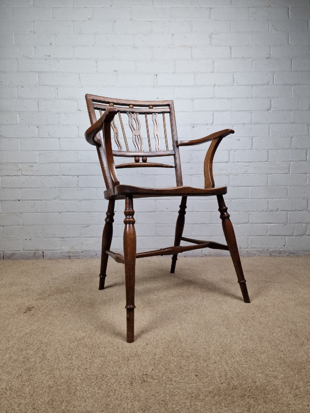 A mid-19th-century wooden Mendlesham armchair featuring a squared backrest with turned wooden spheres, pierced splats, curved arms, and a shaped seat on turned legs. View IX
