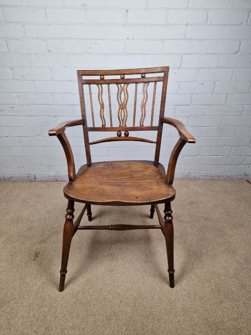 A mid-19th-century wooden Mendlesham armchair featuring a squared backrest with turned wooden spheres, pierced splats, curved arms, and a shaped seat on turned legs. View X