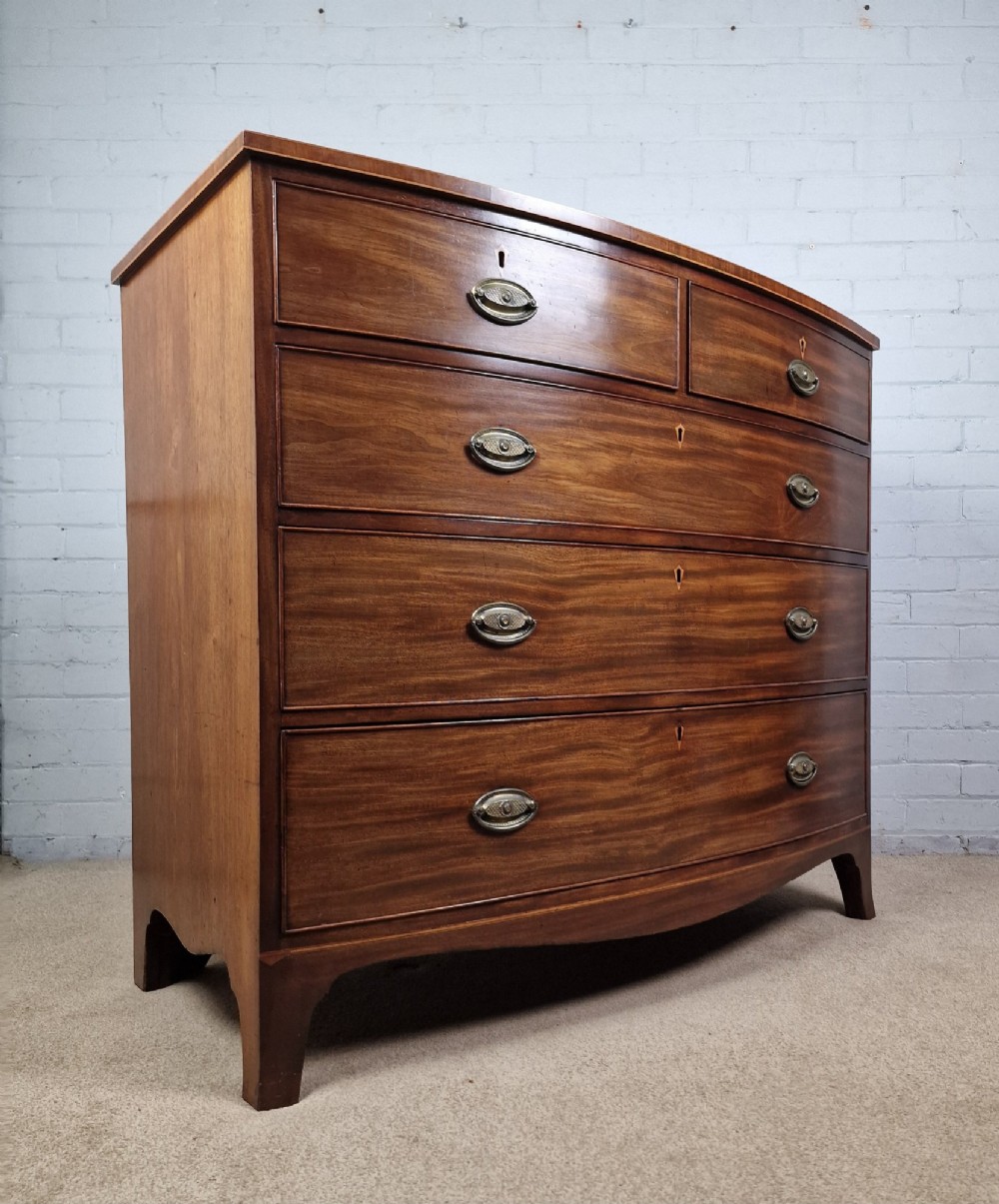 A George III mahogany bowfront chest of drawers featuring two short over three long graduating drawers with brass handles and splay bracket feet. View II