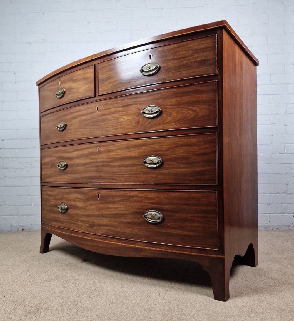 A George III mahogany bowfront chest of drawers featuring two short over three long graduating drawers with brass handles and splay bracket feet. View III