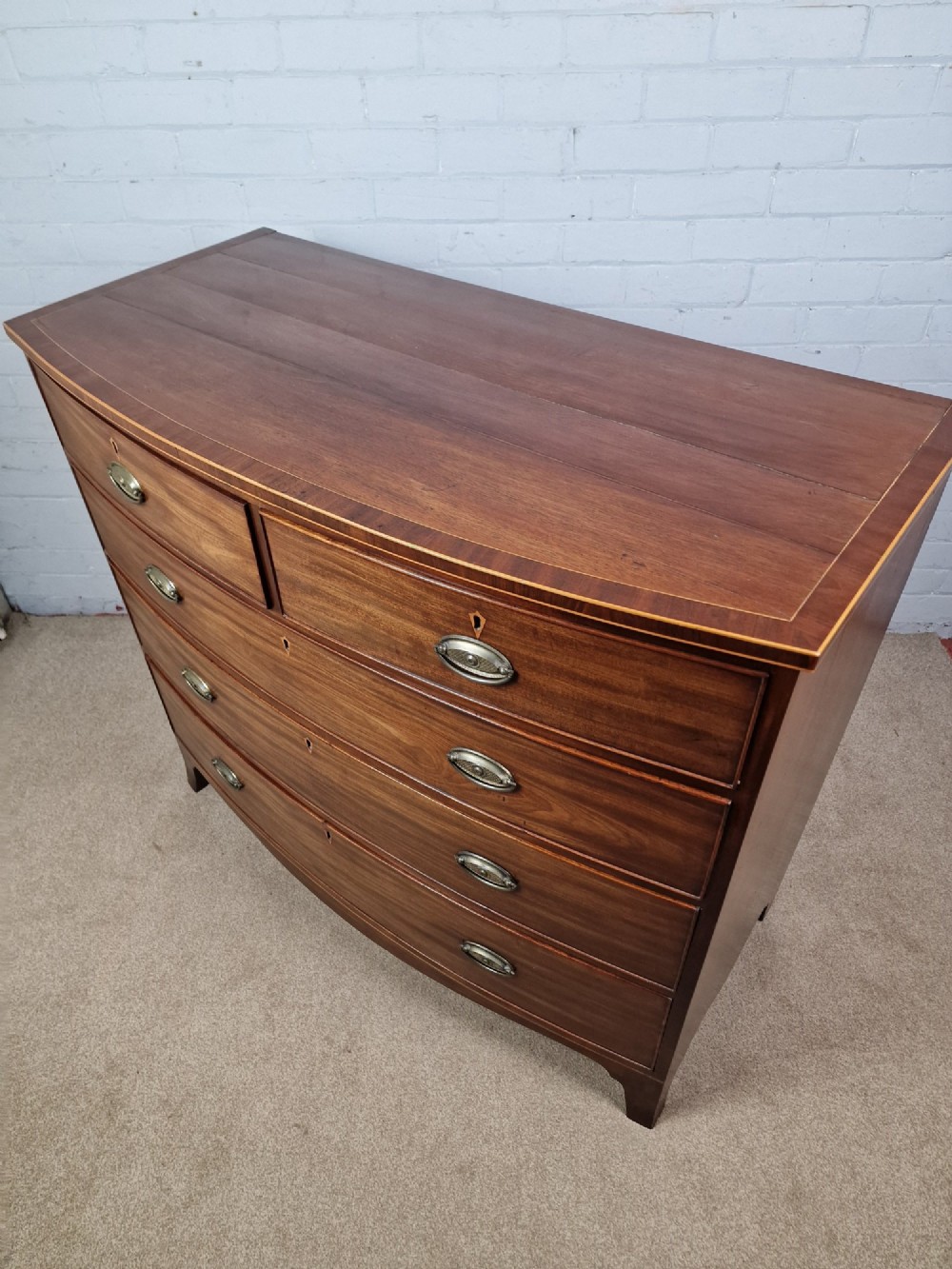 A George III mahogany bowfront chest of drawers featuring two short over three long graduating drawers with brass handles and splay bracket feet. View IV