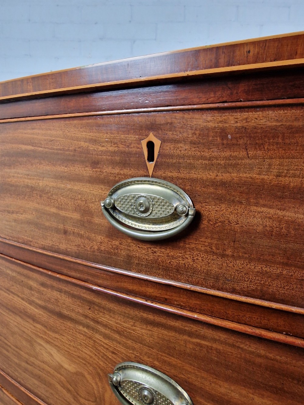 A George III mahogany bowfront chest of drawers featuring two short over three long graduating drawers with brass handles and splay bracket feet. View V