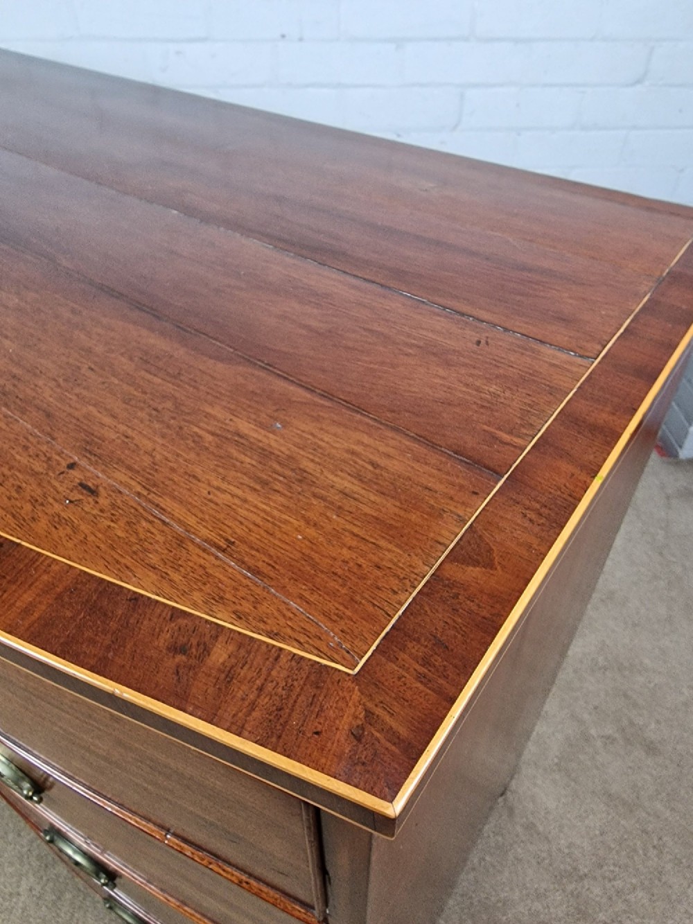 A George III mahogany bowfront chest of drawers featuring two short over three long graduating drawers with brass handles and splay bracket feet. View VII