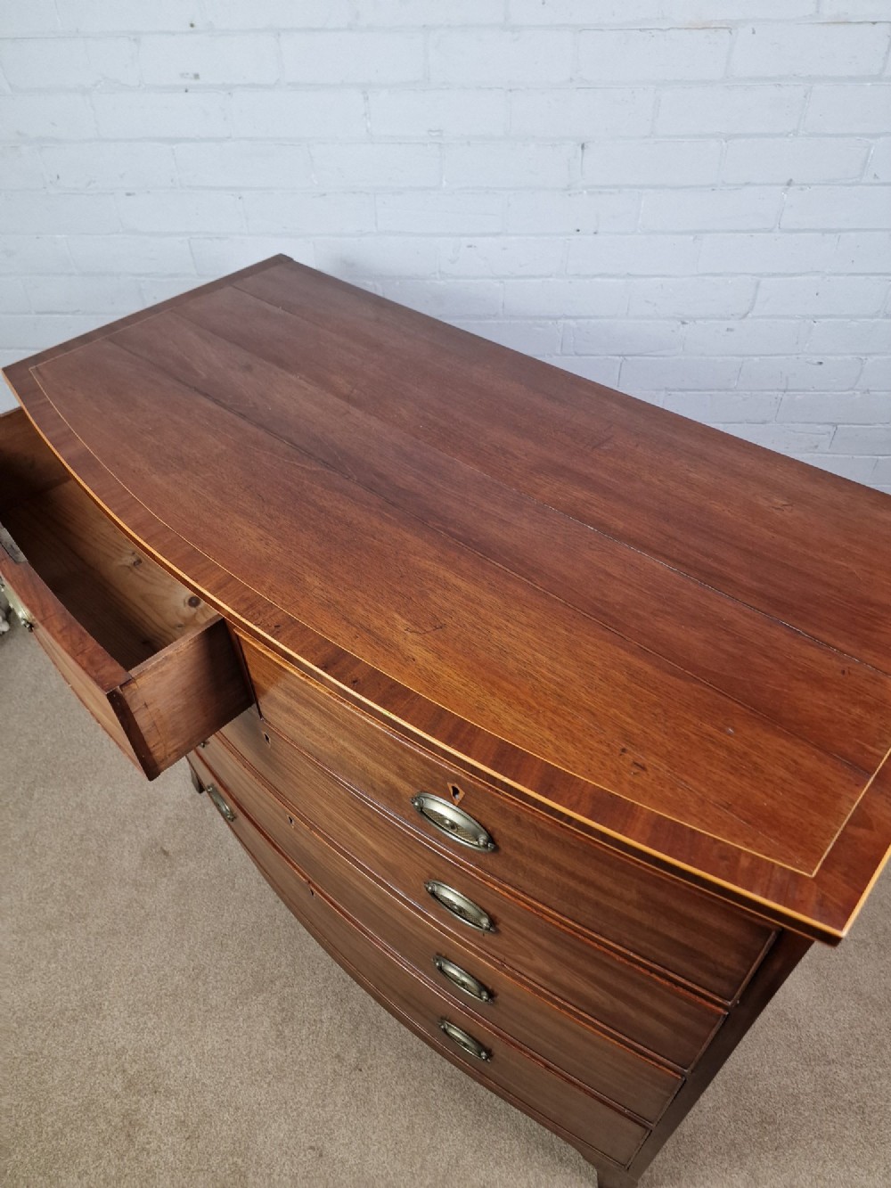 A George III mahogany bowfront chest of drawers featuring two short over three long graduating drawers with brass handles and splay bracket feet. View VIII