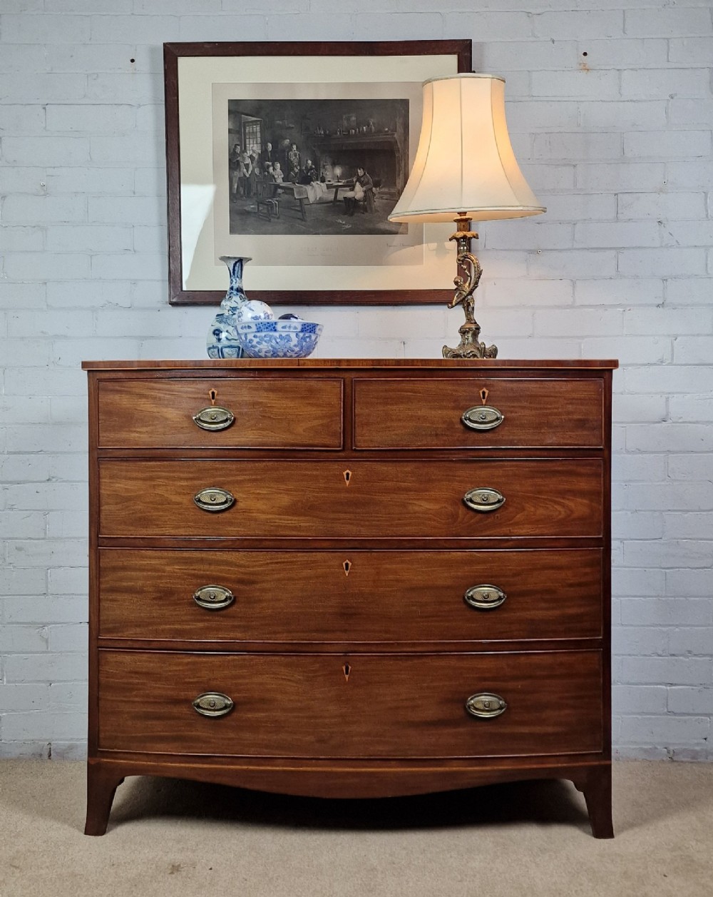 A George III mahogany bowfront chest of drawers featuring two short over three long graduating drawers with brass handles and splay bracket feet.