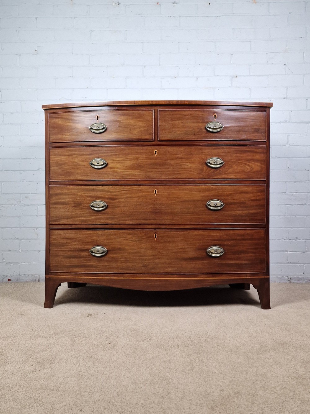A George III mahogany bowfront chest of drawers featuring two short over three long graduating drawers with brass handles and splay bracket feet. View X
