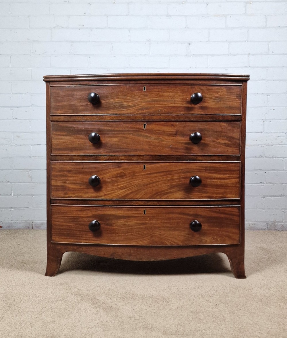 A George III mahogany bow front chest of drawers featuring four graduated drawers with dark turned wooden handles and splayed bracket feet. View II