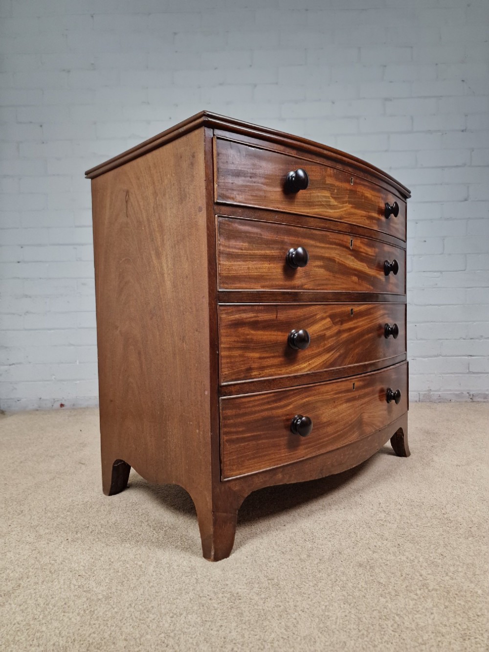 A George III mahogany bow front chest of drawers featuring four graduated drawers with dark turned wooden handles and splayed bracket feet. View V