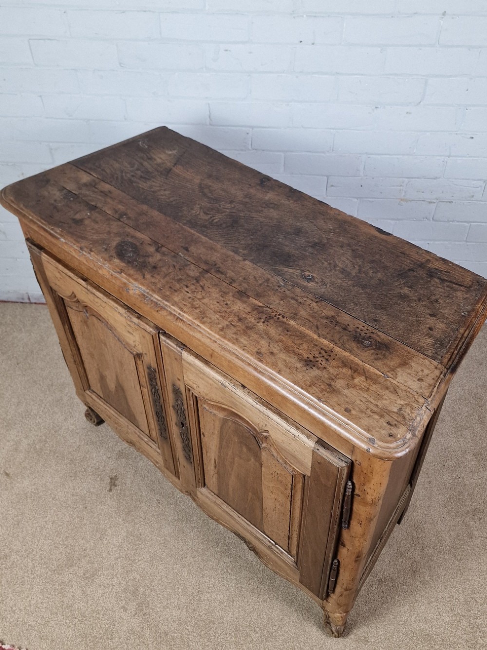 An antique French provincial two-door wooden side cabinet featuring carved panel doors, iron escutcheons, and short cabriole legs. View II