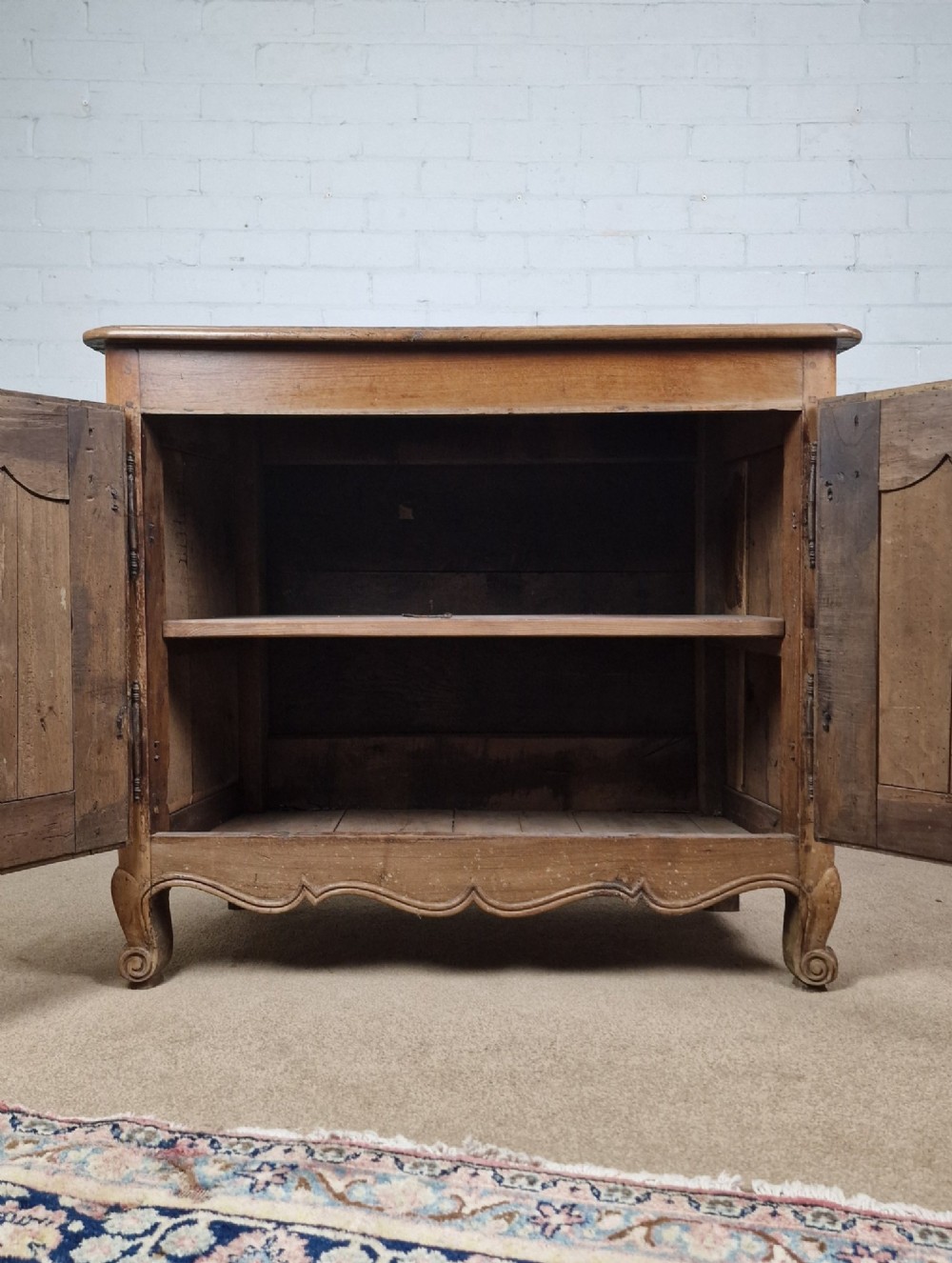 An antique French provincial two-door wooden side cabinet featuring carved panel doors, iron escutcheons, and short cabriole legs. View V