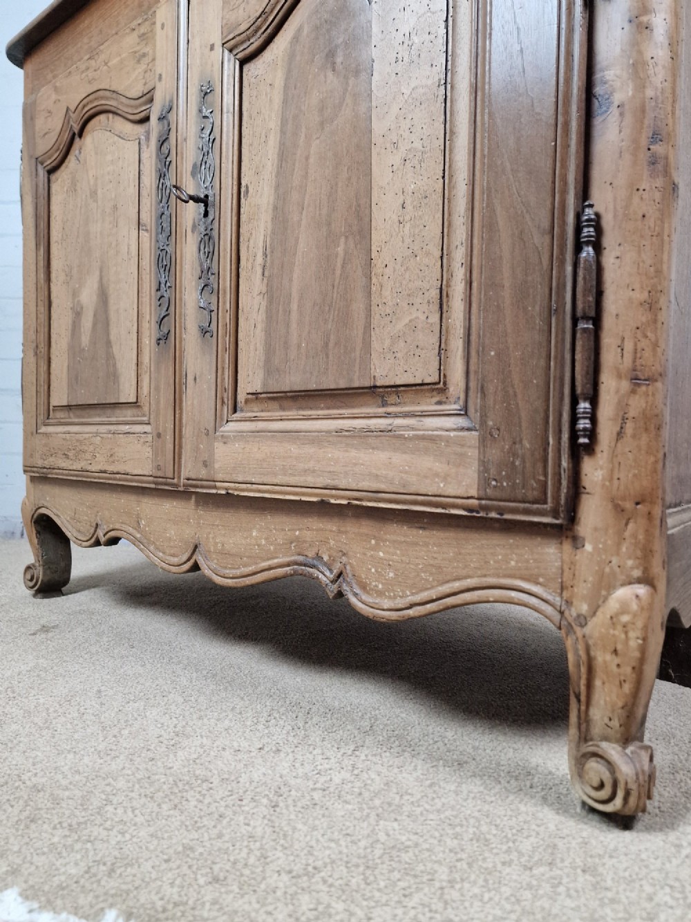 An antique French provincial two-door wooden side cabinet featuring carved panel doors, iron escutcheons, and short cabriole legs. View VII