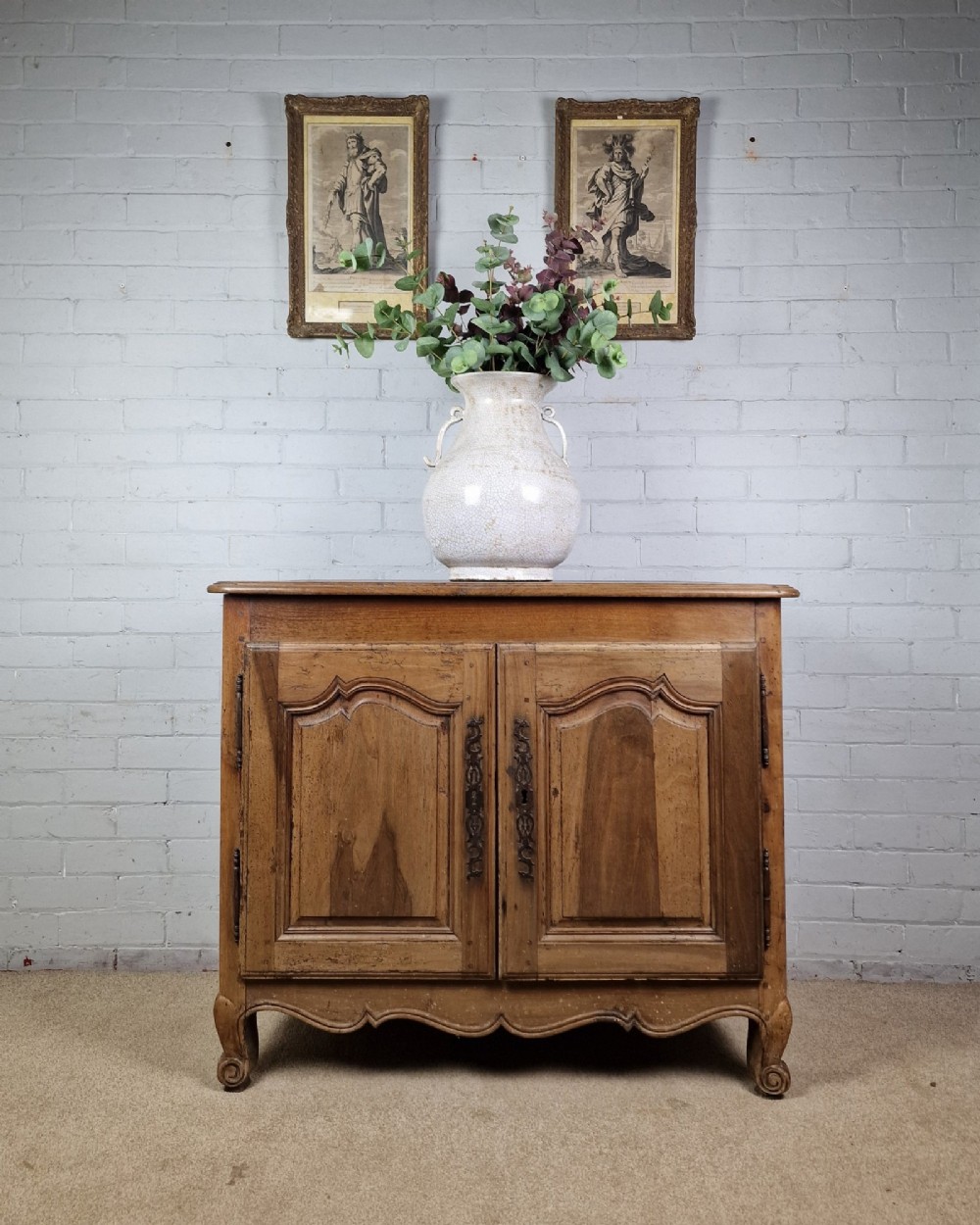 An antique French provincial two-door wooden side cabinet featuring carved panel doors, iron escutcheons, and short cabriole legs. View IX