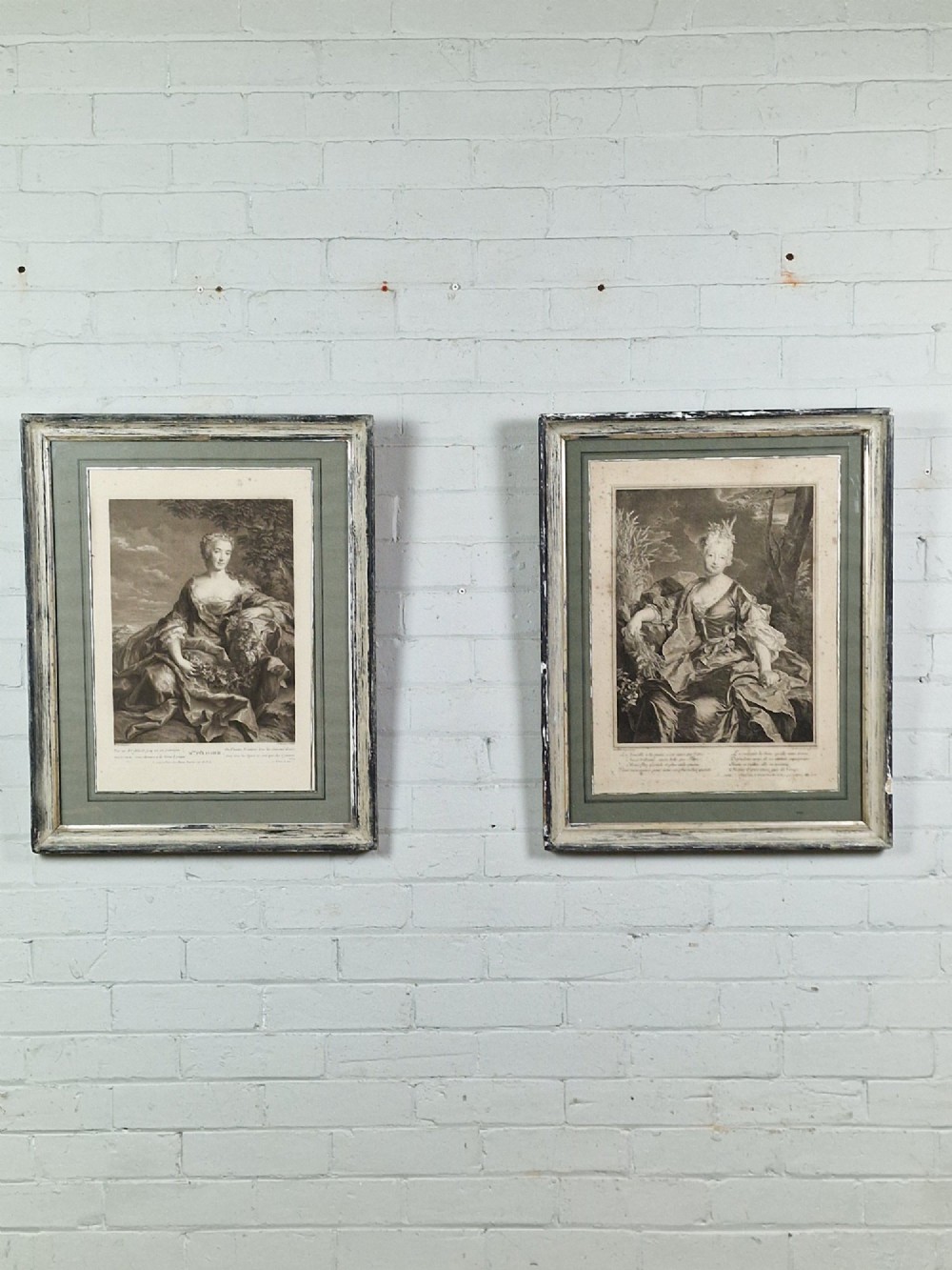 A pair of framed 18th-century French portrait engravings featuring seated female figures, presented in distressed wooden frames with green and cream double mounts.