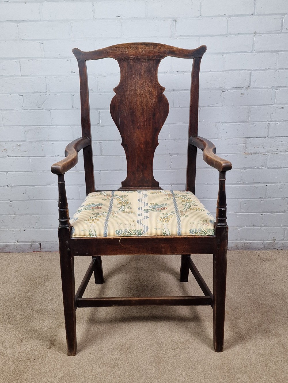 A late eighteenth-century dark oak armchair featuring a vase-shaped splat back, turned arm supports, and a patterned floral fabric drop-in seat.