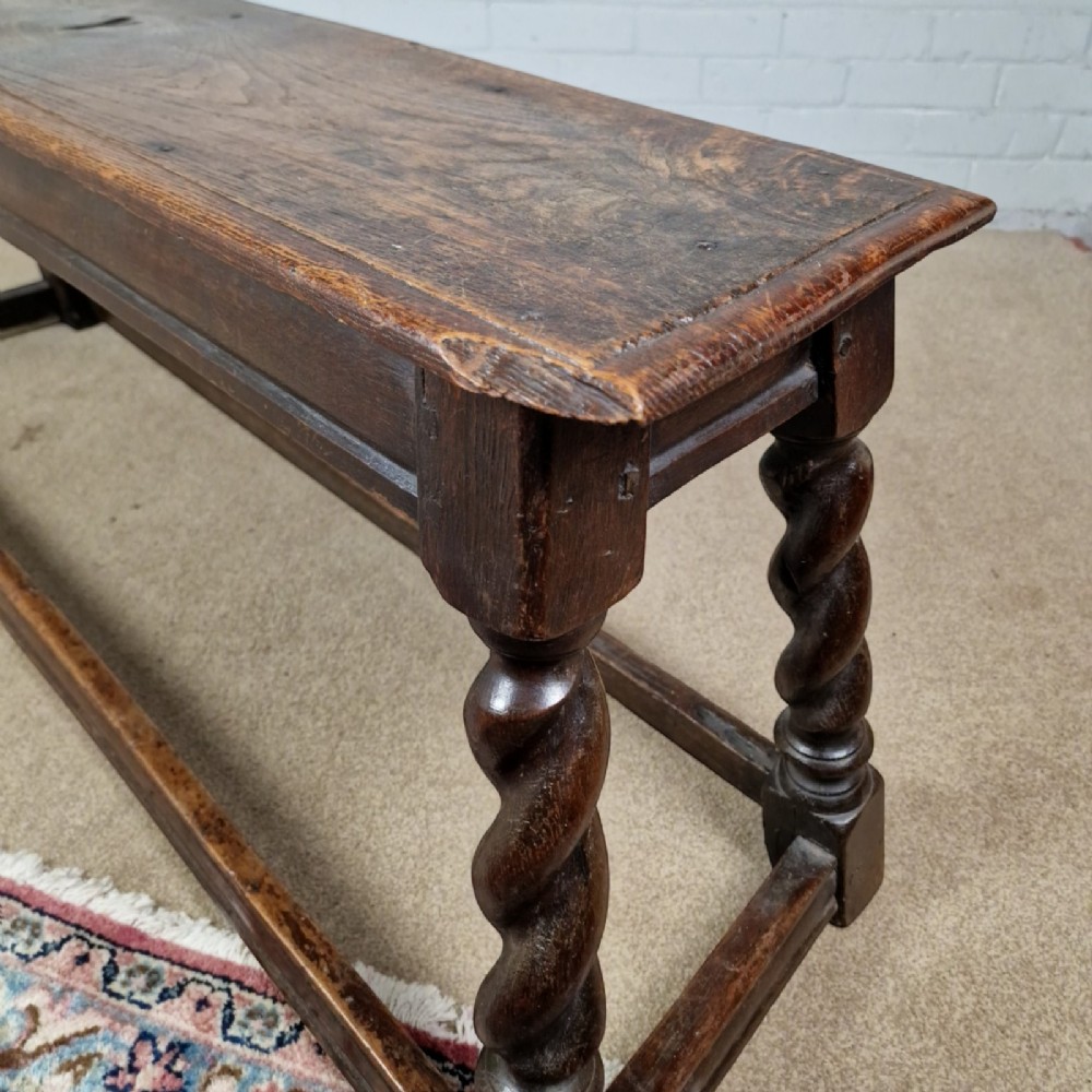An 18th-century dark oak long stool featuring four barley twist legs connected by low stretchers beneath a solid rectangular top. View II