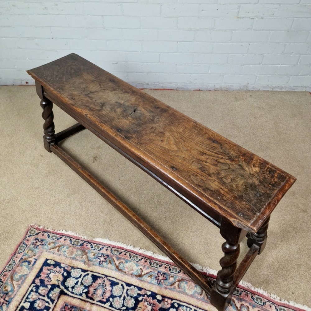An 18th-century dark oak long stool featuring four barley twist legs connected by low stretchers beneath a solid rectangular top. View IV