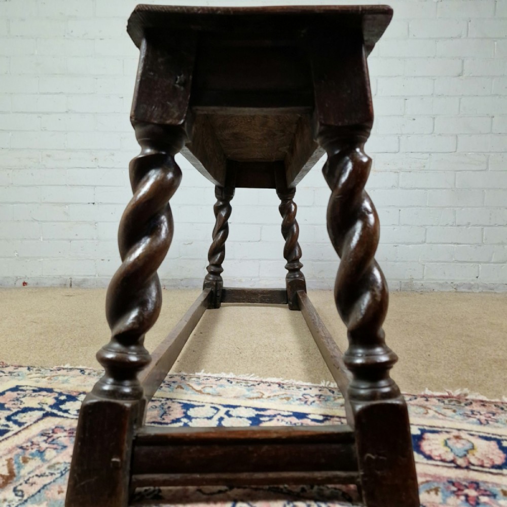 An 18th-century dark oak long stool featuring four barley twist legs connected by low stretchers beneath a solid rectangular top. View VI